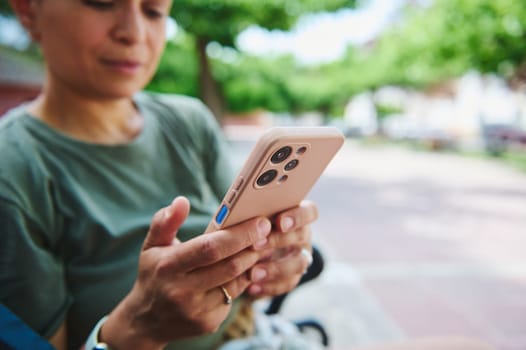 An individual interacts with a smartphone while seated outdoors in a sunlit park, illustrating modern technology usage and communication.