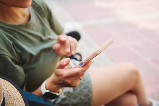 A person is seen relaxing in an outdoor setting, using a smartphone. The scene captures a moment of connection with technology during leisure under natural sunlight.