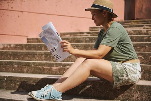 Casually dressed woman enjoys reading a newspaper while seated on outdoor stone steps, exuding relaxation and a tranquil urban atmosphere.