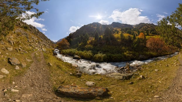 Low angle view upstream along a rushing river in Zhylamysh Gorge, Kyrgyzstan. Banks display vibrant autumn foliage and conifers below steep mountains.