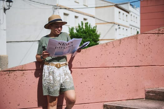 A casual moment outdoors as a woman in a hat and summer attire reads a newspaper against a bright wall under the sunlight, exuding relaxation and leisure.