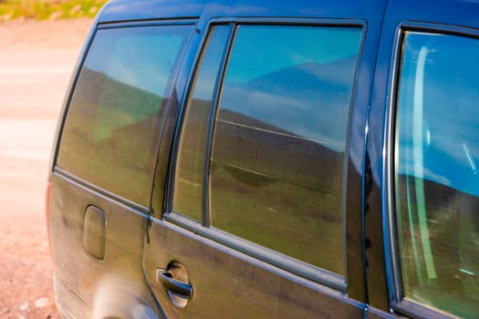 Rear view of a black vehicle covered in dust, with tinted windows reflecting the outdoor surroundings.