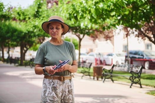 A woman in casual summer attire enjoys a sunny day at a beautiful park, surrounded by trees and benches along a pedestrian pathway.