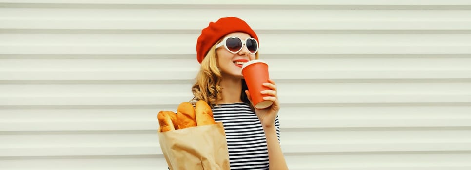 Beautiful happy smiling woman holding grocery shopping paper bag with fresh long white bread baguette, cup of coffee wear red french beret on white background