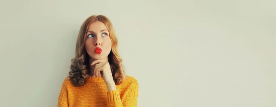 Portrait of beautiful pensive caucasian young woman thinks looking up on studio background, girl blowing her lips with red lipstick, blank copy space