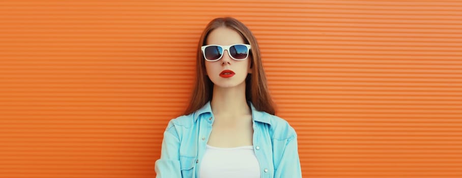 Portrait of modern stylish young woman in white glasses, casual clothing posing on vivid orange wall background