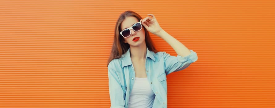 Portrait of modern stylish young woman in white glasses, casual clothing posing on vivid orange wall background