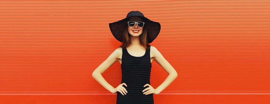 Summer portrait of beautiful stylish young woman posing in black straw hat, glasses, dress on bright red background