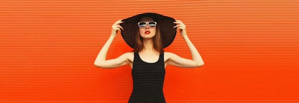 Summer portrait of beautiful stylish young woman posing in black straw hat, glasses, dress on bright red background