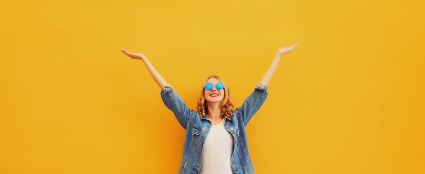 Summer holidays, inspired happy cheerful smiling young woman raising her hands up wearing denim clothing, glasses on colorful yellow background