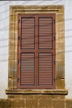 Classic Mediterranean-style window with wooden shutters on a whitewashed wall in a Cypriot village.