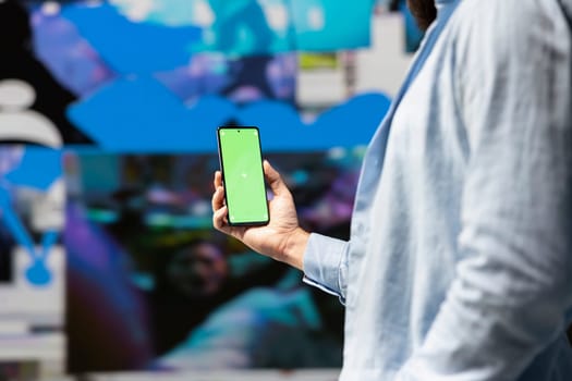 Male influencer holds phone with chroma key screen for online presence, using his imagination and storytelling skills to connect with followers and boost online engagement. Modern web design.