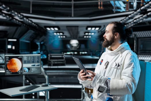 Cosmonaut in orbital station using tablet to verify navigation coordinates towards Mars. Man working on orbital station analyzing mission logs and doing Martian surface research