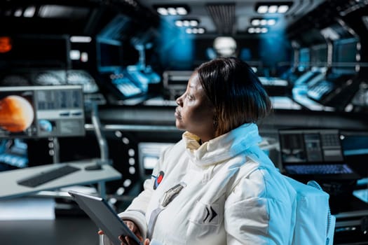 Woman in orbital station analyzing Mars planetary information on tablet. African american spaceship crew member doing Martian surface research using device to assist future planetary exploration