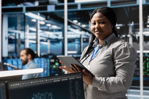 Portrait of smiling data center programmer using tablet to update servers tech, configuring gear using software tools. Happy server farm worker reviewing hardware analytics using device