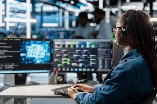 Data center support expert talking in headset microphone, supporting engineering team doing equipment maintenance. Employee in server farm coordinating technicians using mic