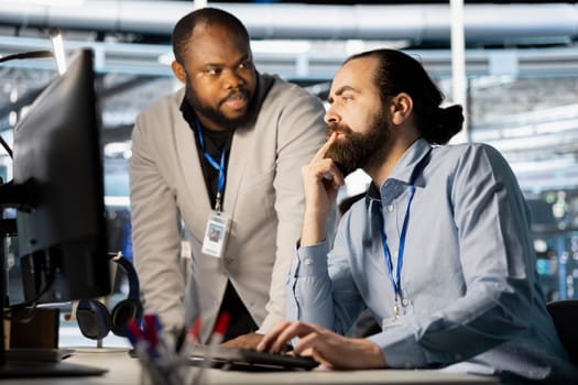 Data center manager supervising work done by employee verifying neural network parameters. Server hub supervisor overseeing worker inspecting configurations to ensure optimal performance