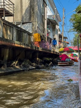 Bangkok, Thailand - November 12, 2024: Thai market vendor selling fresh produce on a sailboat, traditional floating market scene where tourists buy exotic fruits and vegetables from a boat.