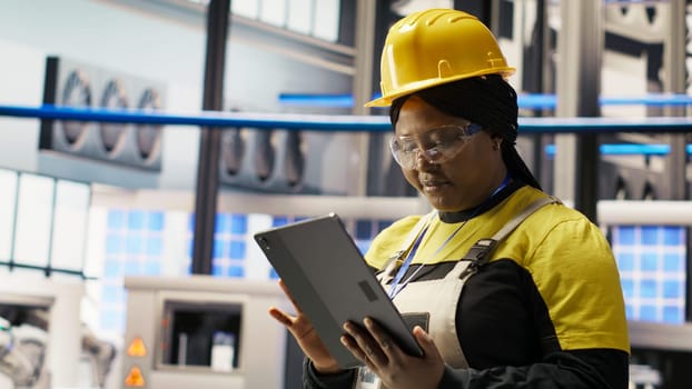 Smiling engineer in smart factory performing predictive maintenance using tablet, analyzing IoT sensor data. Industrial plant worker managing operational reliability of photovoltaic systems, camera B