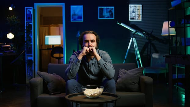 Disappointed supporter watching sports match on live broadcast, upset by team mistake. Annoyed man at home on couch looking at football competition, dejected by chance missed by player