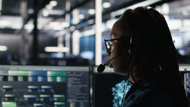 Data center expert examines node tree interface, delivering technical support. Server room technician talking in headset mic with coworkers, using visual programming software, camera B