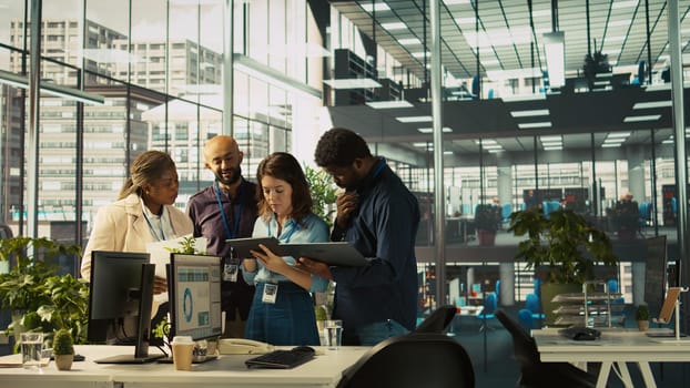 Multiethnic coworkers looking over revenue figures on tablet in diverse office. Multiracial colleagues doing brainstorming, comparing company statistical numbers, working hard to finish job, camera B