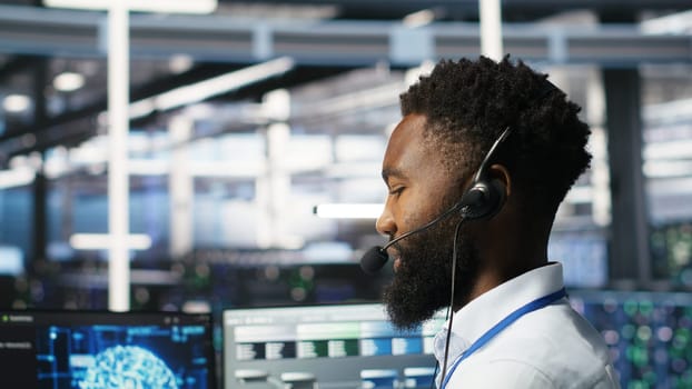 Data center employee talking in headset mic, coordinating technicians setting up hardware for artificial intelligence deployment. Server room worker engages in remote call with engineers, camera B