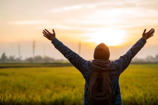 Back view of a man with raised arms in front of green field..