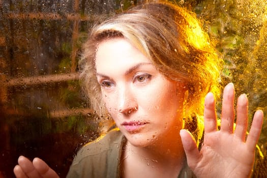 A woman presses her hands against a fogged window, lost in thought as warm light creates a comforting ambiance in the room.