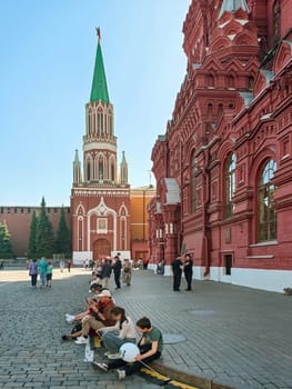 Moscow, Russia - May 28, 2025. People sit and relax near a historic red brick building in Moscow. The scene captures tourists with a curiosity and relaxation, set against the iconic architecture. Made on smartphone.