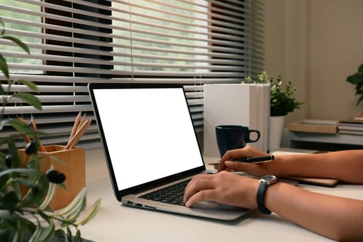 Hands of a person working on a laptop with a blank screen at a modern home office desk.