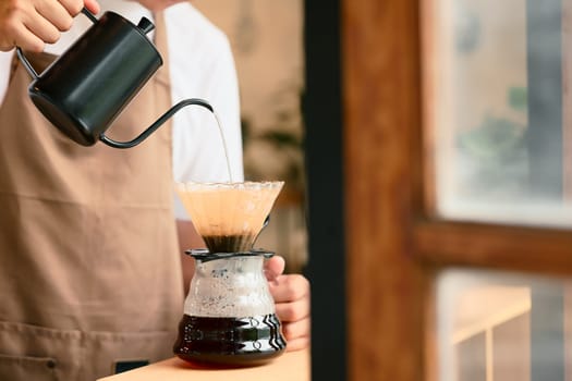 Man pouring hot water into coffee dripper to brew fresh pour over coffee.