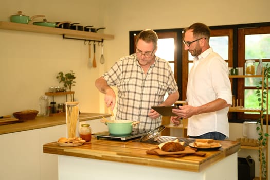 Smiling father and adult son preparing a pasta meal together in a cozy home kitchen. Father day concept.