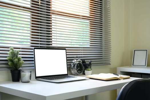 Minimalist home office setup with a laptop, notebook, and alarm clock near a window.
