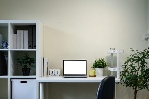 Organized home office workspace with blank screen laptop, indoor plants, and minimalist calendar.