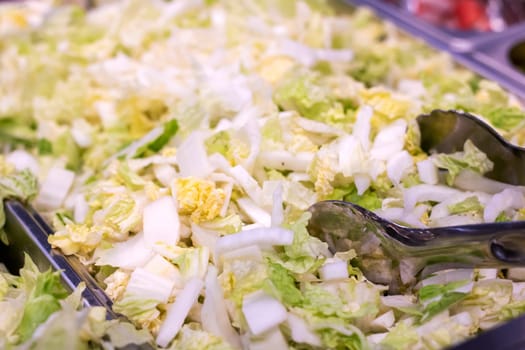 A detailed closeup view of a vibrant salad featuring an assortment of fresh ingredients, with tongs placed strategically within it