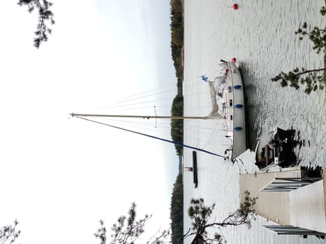 A sailboat is moored to a wooden pier in the harbor of Baltic sea, Gulf of Finland. The boat is securely tied with ropes, gently floating on calm water with finish flag