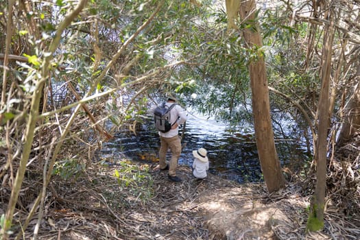 Father and son enjoying a peaceful moment by the river, surrounded by lush vegetation, observing the flowing water