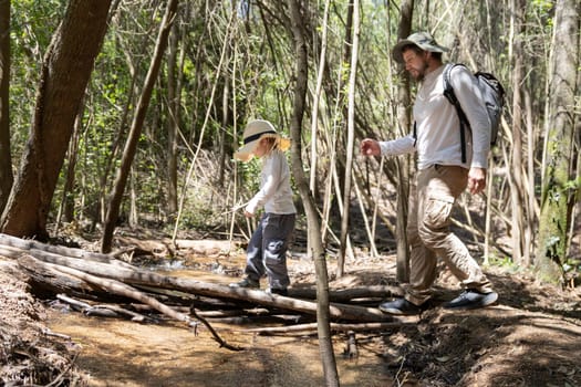 Father and son carefully crossing a small creek while hiking in a sunny forest