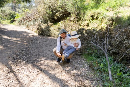 Father crouching and helping his son to put on his shoe while hiking in a forest