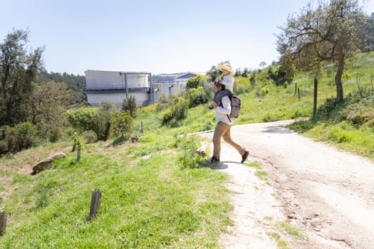 Father carrying daughter on shoulders while walking on country road near water treatment plant