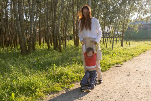 Happy mother swinging her son in a forest path during a sunny day