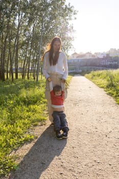 Mother swinging her son along a path in a park during sunset