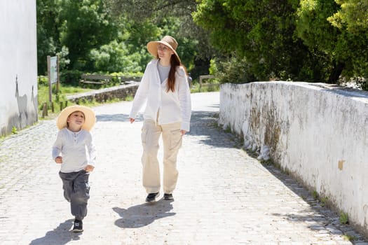 Mother and son enjoying a walk on a cobblestone street during a sunny day