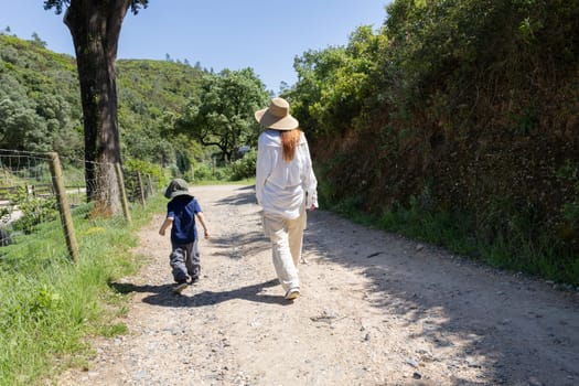 Mother and son enjoying a leisurely stroll along a sunny country road, surrounded by lush greenery