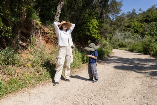 Mother and son wearing hats are hiking in nature on a sunny summer day