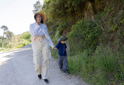 Mother talking on smartphone while walking with her son on a path through nature