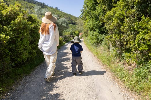 Mother and son wearing hats are walking down a gravel road on a summer day