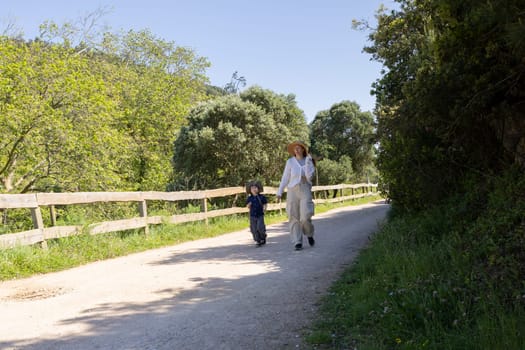 Mother and son enjoying a leisurely walk on a sunny spring day, surrounded by lush greenery and a wooden fence