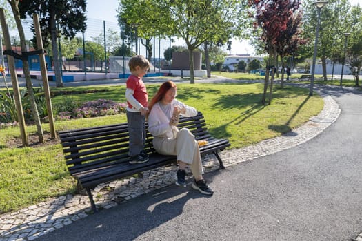 Mother disinfecting hands while sharing a snack with her son on a park bench